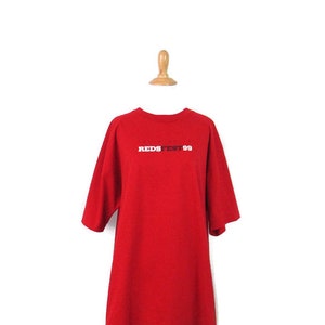 May include: Red short-sleeved t-shirt with the text "REDSTEST 99" printed on the front in white and black.