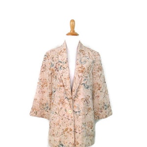 May include: A beige blazer with a floral pattern. The blazer has a button closure and long sleeves.