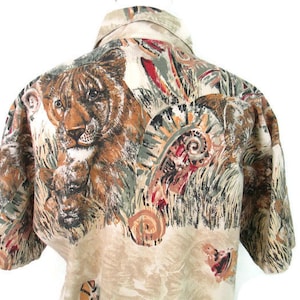May include: A beige short-sleeved button-up shirt with a colorful print of tigers, leaves, and abstract patterns.