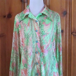May include: A long-sleeved, button-up shirt with a green, pink, and white abstract print. The shirt has a collar and a button-up front.