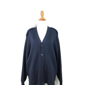 May include: A dark blue cardigan with a v-neck and button closure. The cardigan has long sleeves and a ribbed hem.