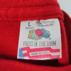 Pu&ograve; includere: Un'etichetta bianca con accenti rossi, blu e verdi. L'etichetta dice "Fruit of the Loom" e "100% Cotone Pre-Ristretto" con un piccolo logo di un grappolo d'uva e una mela rossa. L'etichetta dice anche "Adulto" e "L" e "Made in U.S.A."