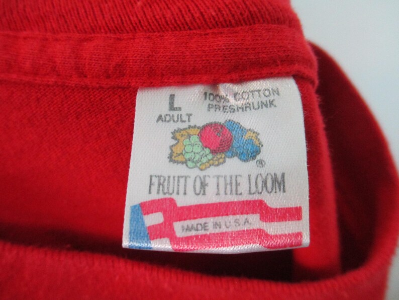 Pu&ograve; includere: Un'etichetta bianca con accenti rossi, blu e verdi. L'etichetta dice "Fruit of the Loom" e "100% Cotone Pre-Ristretto" con un piccolo logo di un grappolo d'uva e una mela rossa. L'etichetta dice anche "Adulto" e "L" e "Made in U.S.A."