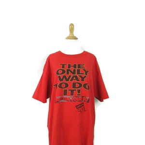 Puede incluir: Camiseta roja con un gráfico negro que dice "The Only Way To Do It!" con el logotipo de Levi's 501 debajo.
