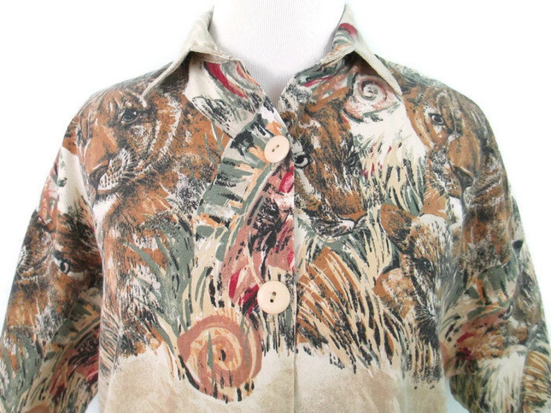 May include: A beige button-up shirt with a short sleeve and a print of brown and black animal faces on a beige background.