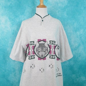 Op de afbeelding: Grijs T-shirt met korte mouwen met een wolf-print en voetafdrukken. Het shirt heeft een mandarijnskraag en een knoopsluiting. De tekst "Sol Duc Hot Springs" staat gedrukt op de rechteronderkant van het shirt.