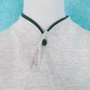 Op de afbeelding: Een grijs longsleeve shirt met een groene kraag en een enkele knoopsluiting aan de hals.
