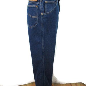 Pode incluir: Jeans de denim azul escuro com um remendo de couro marrom que diz "Lee" na parte de tr&aacute;s da cintura.
