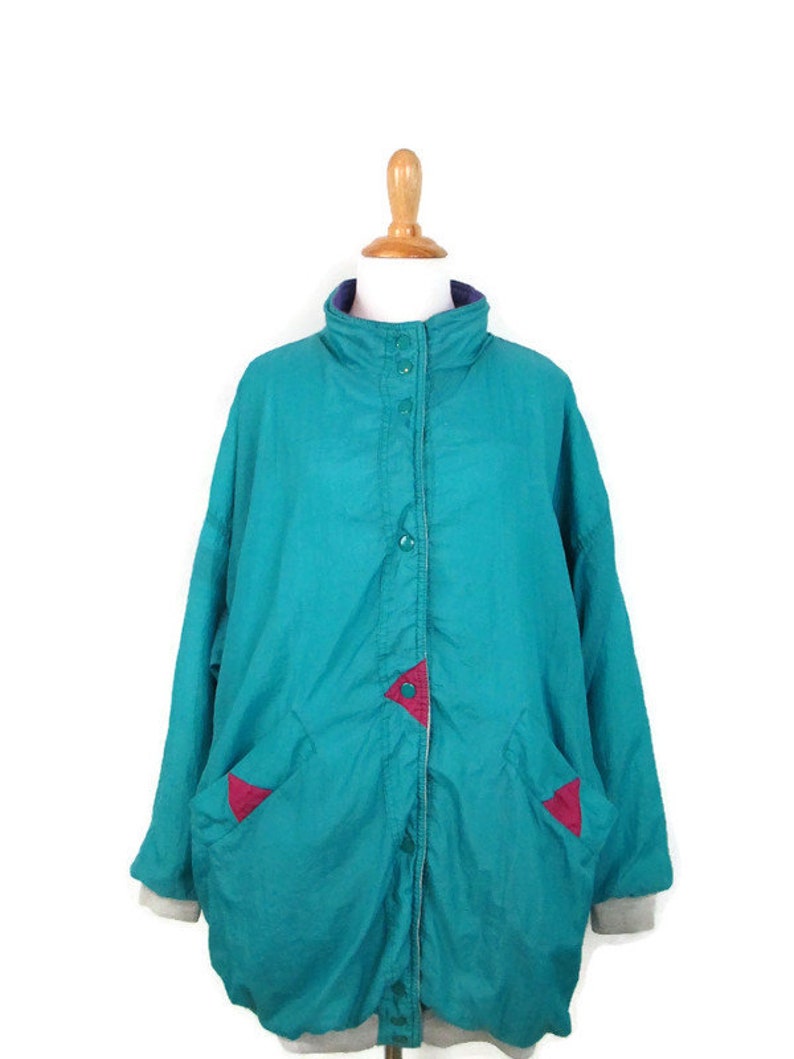 May include: A teal blue jacket with a snap closure and two pockets. The jacket has red and purple accents on the pockets and collar.