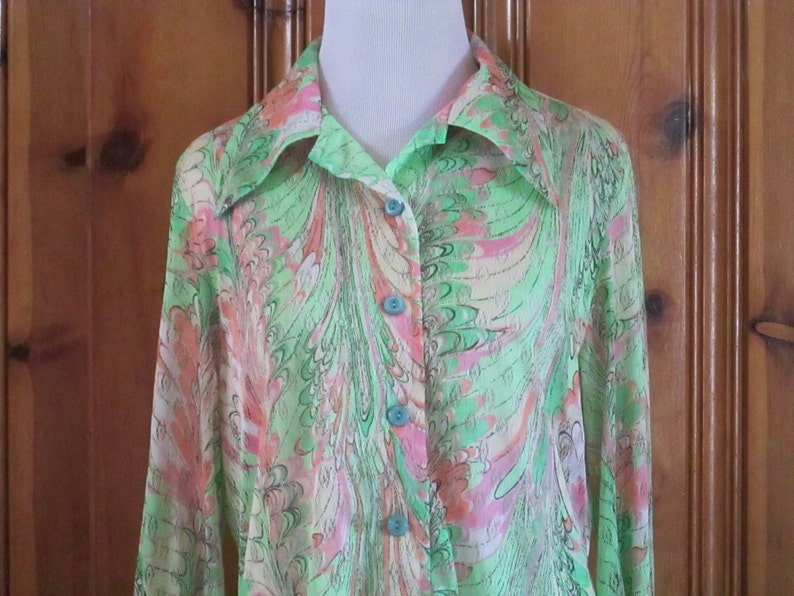 May include: A long-sleeved, green, pink, and white patterned shirt with a teal button-up closure.