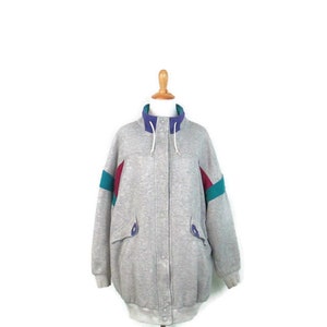 May include: A gray sweatshirt jacket with a zipper closure and a hood. The jacket has colorful accents on the sleeves in shades of teal, purple, and red.