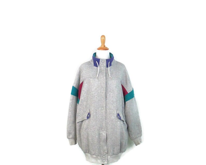 May include: A gray sweatshirt jacket with a zipper closure and a hood. The jacket has colorful accents on the sleeves in shades of teal, purple, and red.