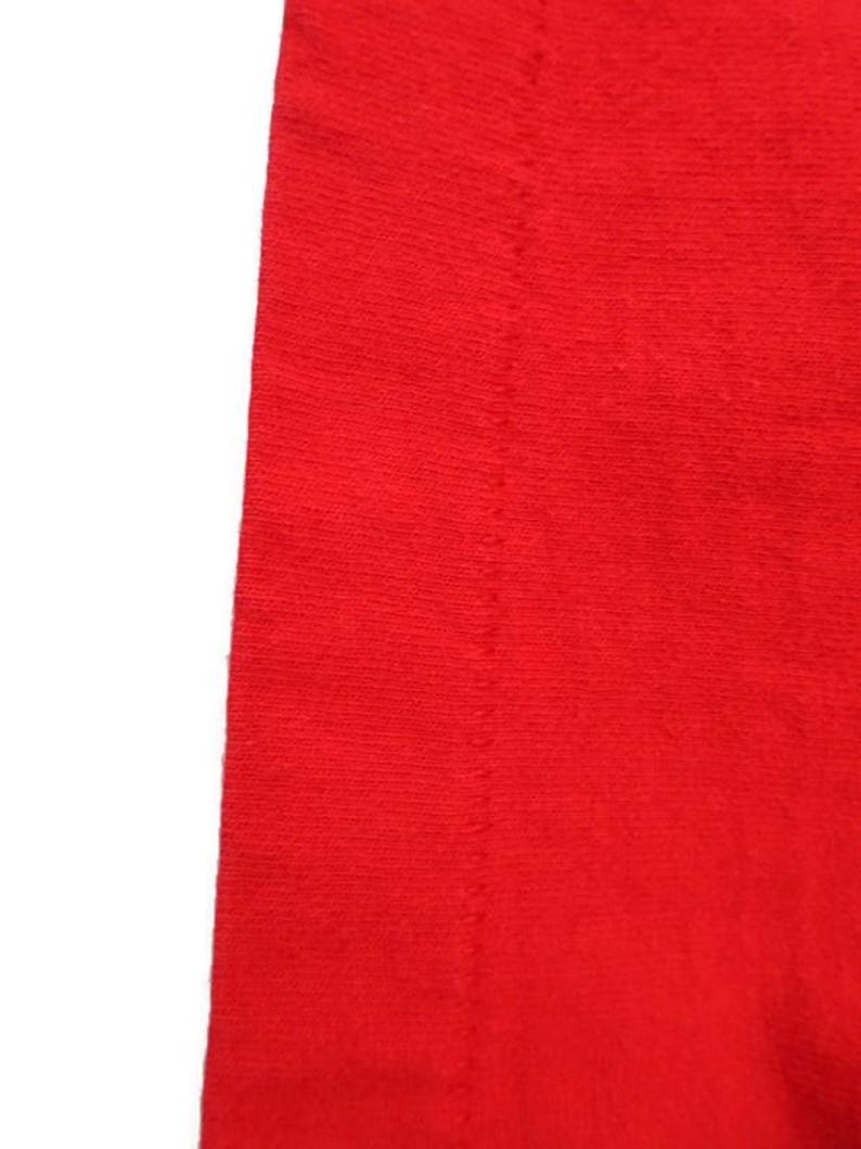 Pu&ograve; includere: Primo piano di un tessuto rosso vivo con una cucitura dritta che corre al centro.