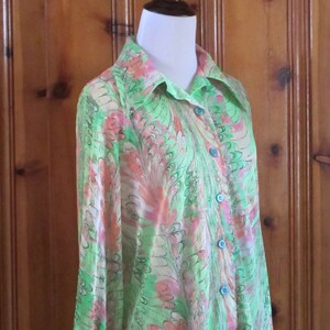 May include: A long-sleeved, green and pink patterned shirt with a collared neckline and blue buttons. The shirt is made of a lightweight fabric and has a flowing silhouette.