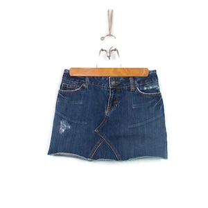 Puede incluir: Una minifalda vaquera azul con detalles desgastados y un dobladillo deshilachado.