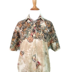 May include: A beige button-up shirt with a short sleeve and a colorful animal print. The print features a variety of animals, including lions, tigers, and leopards.