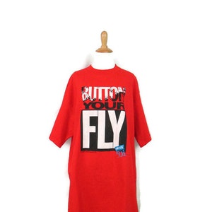 Puede incluir: Camiseta roja con un gráfico en blanco y negro que dice "Button Up Your Fly".