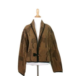 May include: A brown jacket featuring a repeating black zebra pattern, long sleeves, a shawl collar, and a single toggle closure at the front. The garment is finished with black trim along the edges and is displayed on a mannequin.