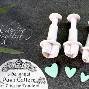 May include: Three white plastic heart-shaped push cutters with a green fondant heart next to each cutter. The cutters are labeled "3 Delightful Push Cutters for Clay or Fondant".