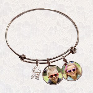 May include: A rose gold-toned expandable bangle bracelet featuring three dangling charms: a silver-toned metal charm shaped like the word love and two circular photo charms, one showing a boy in red sunglasses and one showing a girl in pink sunglasses.