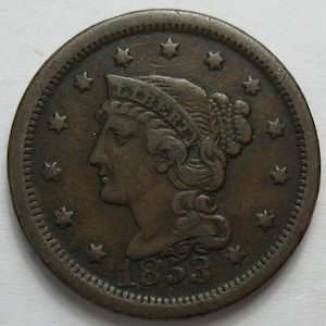 May include: A bronze coin featuring a profile of a woman's head, surrounded by stars. The word "LIBERTY" is visible above the head, and the year "1853" is inscribed below. The coin has a worn, antique appearance.