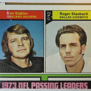 May include: A 1973 NFL Passing Leaders trading card featuring Ken Stabler of the Oakland Raiders and Roger Staubach of the Dallas Cowboys. The card is in good condition with some wear and tear.