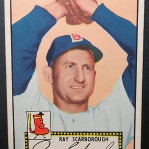 May include: Vintage baseball card featuring Ray Scarborough in a blue cap and jersey, with a baseball glove raised above his head. The card includes the Boston Red Sox logo and Scarborough's name.