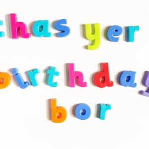 May include: Colourful plastic letters spelling out "Happy Birthday" on a white background.