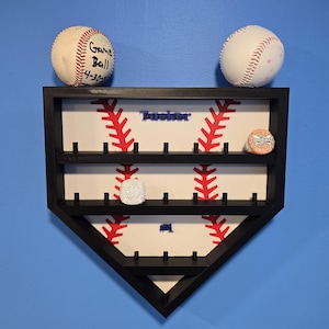 May include: A black baseball-shaped display case with a white interior, red stitching design, and the name "Tucker" in blue. Two baseballs sit on top. The case holds baseballs and other small items.