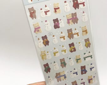 May include: A sheet of stickers featuring illustrations of brown and cream-colored bears and white snowmen wearing colorful scarves and hats. The header text reads Yukidaruma to Kuma and Made in Japan, accompanied by small snowflake and bear icons.