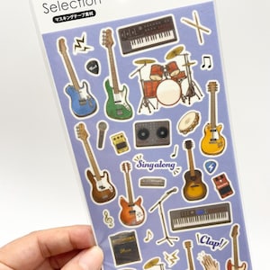 以下が含まれることがあります： エレキギター、アコースティックギター、ドラムセット、キーボード、アンプ、マイク、音符など、様々な楽器が描かれた音楽テーマのステッカーシート。パッケージには「Sticker Selection」および「Made in Japan」という文字が記載されています。