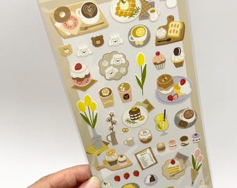May include: A sheet of cafe-themed stickers featuring various illustrations of coffee, pastries, desserts, and flowers. The top of the packaging includes the text & cafe seal and Allured by the pleasant-smelling aroma of coffee, I went into the cafe.