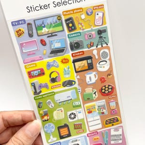 May include: A clear plastic sheet of assorted stickers titled Sticker Selection, featuring colorful illustrations of electronics, kitchen appliances, and beauty tools. The stickers include TVs, computers, cameras, gaming consoles, refrigerators, and hair dryers with Japanese text labels.