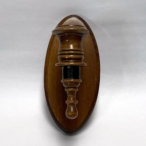 May include: A vintage wooden wall-mounted candle holder. The holder is a dark brown color, with a decorative, turned design. It is mounted on an oval-shaped wooden plaque. The candle holder is approximately 8 inches tall.