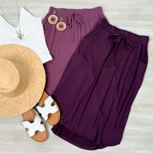 May include: Two skirts, one in a dusty rose color and the other in a deep purple, both with a drawstring waist and a casual, flowy style.