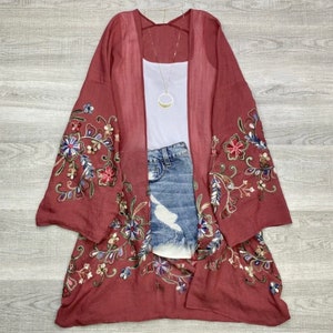 May include: A maroon kimono with floral embroidery. The kimono has a sheer fabric and long sleeves. The embroidery is in shades of blue, green, and gold.