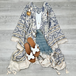May include: A white and blue patterned kimono with a white tank top, denim shorts, and white sandals. The kimono has a yellow floral design.