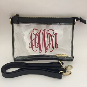 Puede incluir: Bolso cruzado transparente con parte superior y ribete negros, con un monograma burdeos. El bolso tiene cremallera y herrajes dorados, e incluye una correa para el hombro negra. Dise&ntilde;ado para llevar lo esencial.