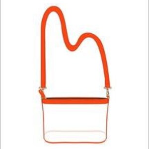 Puede incluir: Un bolso cruzado rectangular transparente con una correa y ribetes naranjas. La correa tiene un dise&ntilde;o curvo &uacute;nico. El bolso cuenta con cierre de cremallera y herrajes plateados. El bolso est&aacute; dise&ntilde;ado para llevarse al hombro.