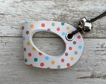 May include: A white, polka-dotted dog toy with a brown cord and a silver metal ring. The toy has a hole in the center and is shaped like a D.