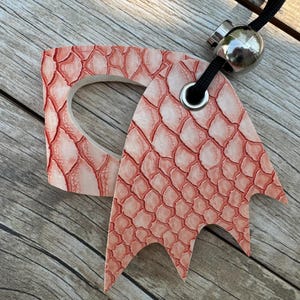 May include: A pink leather key chain with a dragon design. The key chain has a metal ring and a metal bead.