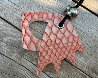 May include: A pink leather key chain with a dragon design. The key chain has a metal ring and a metal bead.