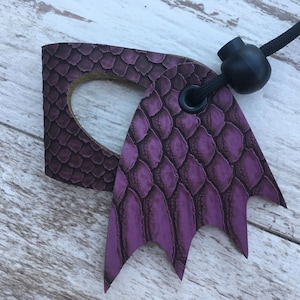 May include: Purple leather key chain with a dragon wing design and a black cord with a black bead.