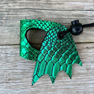 May include: Green dragon-shaped leather key chain with a black cord and a black toggle. The leather has a scaly texture.