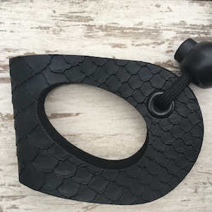 May include: Black rubber leash handle with a textured surface and a black ring. The handle is attached to a black cord with a black ball at the end.