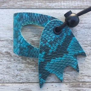 May include: Teal blue leather key chain with a textured snake skin pattern. The key chain has a black cord and a black plastic toggle.