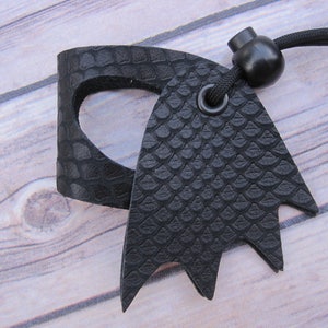 May include: Black leather key chain with a textured snake skin pattern. The key chain has a black cord and a black plastic bead.