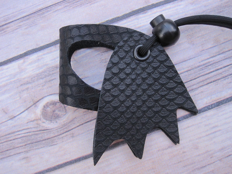 May include: Black leather key chain with a textured snake skin pattern. The key chain has a black cord and a black plastic bead.