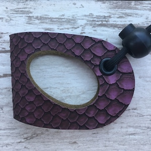 May include: A purple leather dog leash handle with a black cord and a black toggle. The handle has a snakeskin pattern.