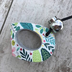 May include: A white leather charm with a floral pattern and a silver metal ring. The charm has a hole in the center and is attached to a black cord.